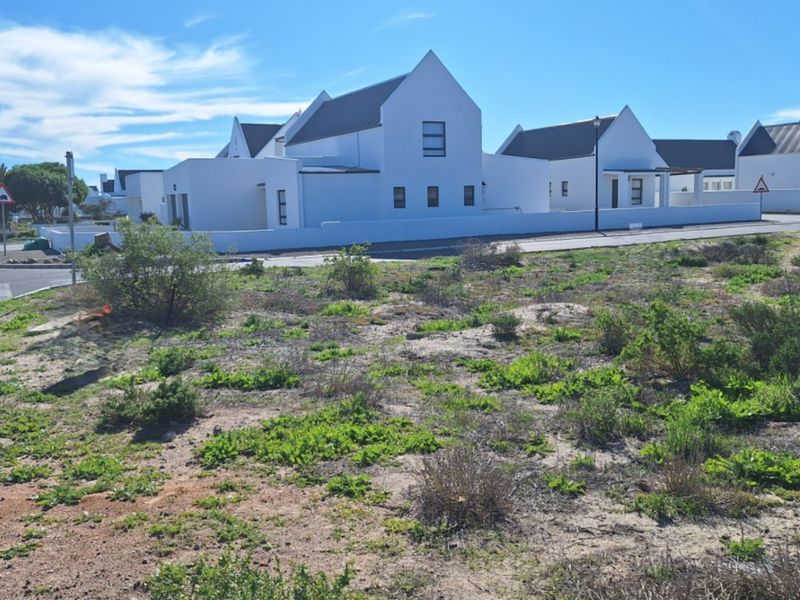 A vacant residential plot situated in a developed estate with paved street access and surrounding modern white homes.