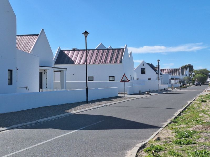 A clear street view of a residential estate featuring modern white homes with metal roofs and paved roads.