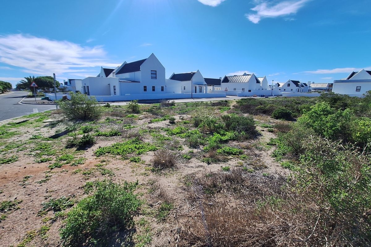 A vacant residential plot situated in a developed estate, featuring natural vegetation and adjacent to a paved street with established neighboring homes.