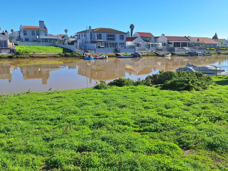 A scenic view of a waterfront residential area featuring a grassy foreground and canal-side properties.