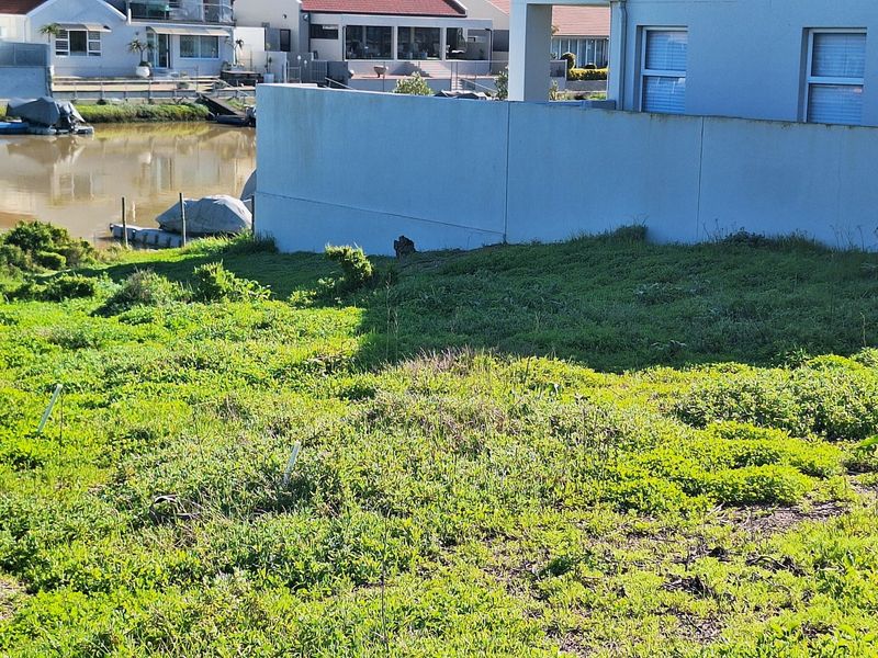 A vacant residential plot featuring a grassy slope, a concrete retaining wall, and direct access to the adjacent waterway.