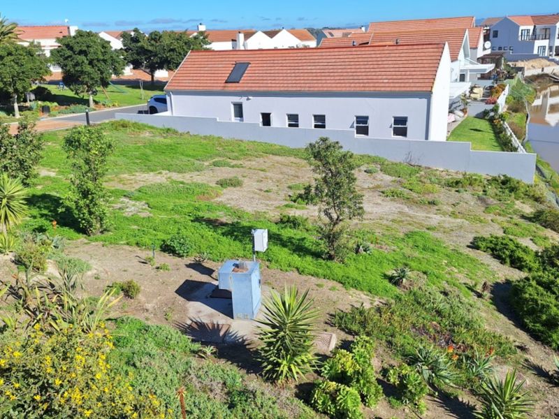 Aerial view of a vacant residential plot featuring established vegetation, an electrical utility box, and direct waterfront access in a developed estate.