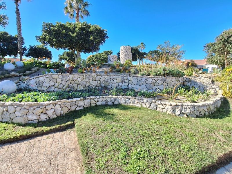 A well-maintained residential garden featuring tiered stone retaining walls, established landscaping, and a paved walkway.