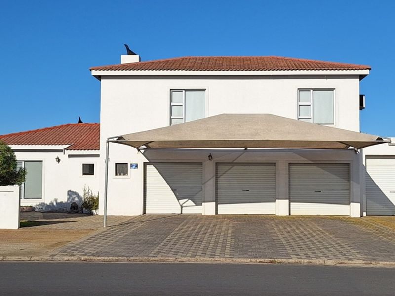 Front elevation of a residential property featuring a triple garage with roller shutter doors, a paved driveway, and a shade sail carport.