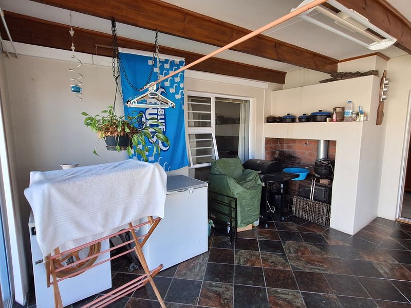 Covered patio area featuring a built-in braai, exposed timber ceiling beams, and tiled flooring, providing a functional outdoor entertainment space.