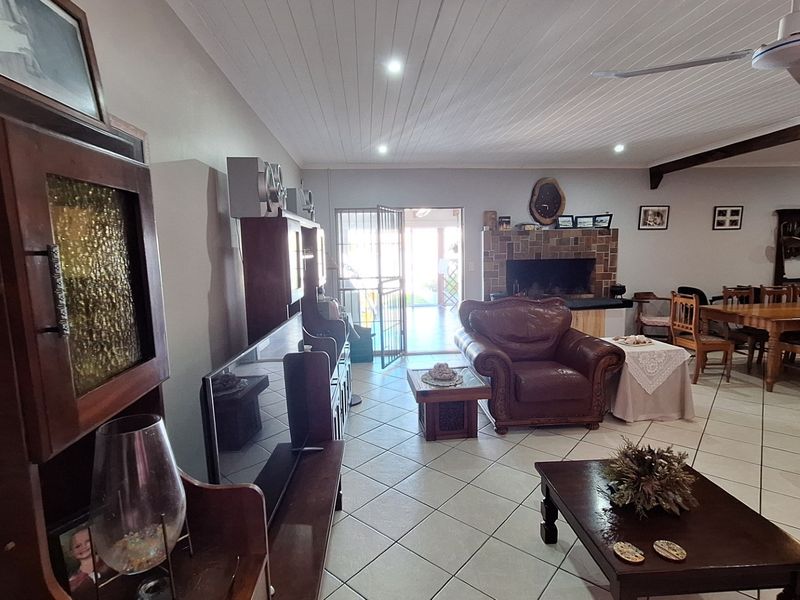 Spacious open-plan living and dining area featuring tiled floors, a brick fireplace, and a timber-clad ceiling with integrated lighting.