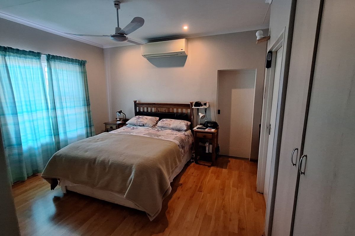 A well-maintained bedroom featuring laminate flooring, a ceiling fan, a split-system air conditioner, and built-in storage cupboards.