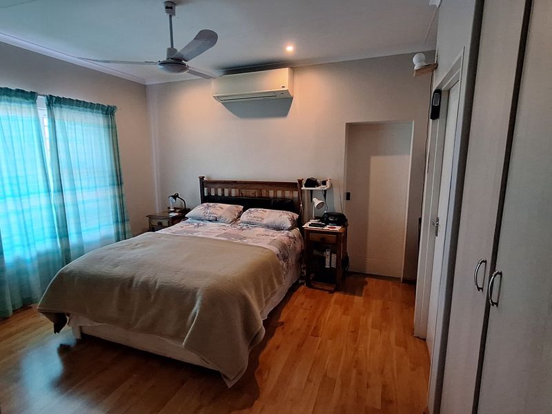 A well-maintained bedroom featuring laminate flooring, a ceiling fan, a split-system air conditioner, and built-in storage cupboards.