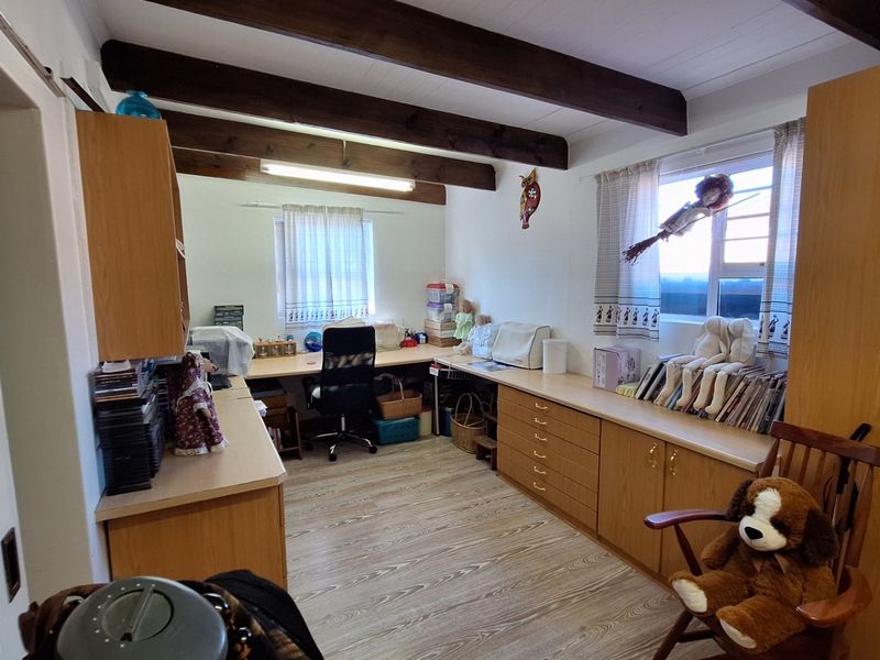 A functional home office featuring built-in desk space, extensive cabinetry for storage, exposed timber ceiling beams, and durable laminate flooring.