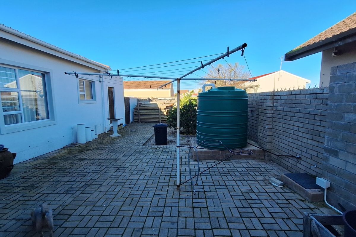 A paved rear courtyard area featuring a brick boundary wall, a water storage tank, and a rotary clothesline.