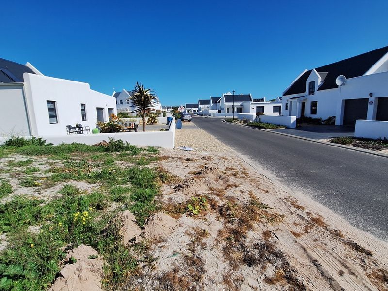 A street view of a residential estate featuring paved roads and established white-walled homes in a coastal setting.