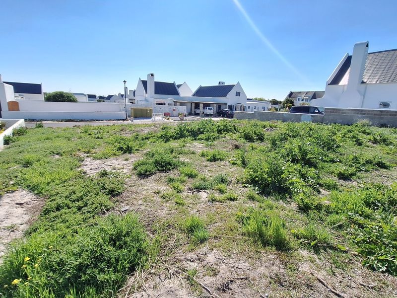 A vacant residential plot featuring natural vegetation and perimeter boundary walls, situated within a developed residential estate.