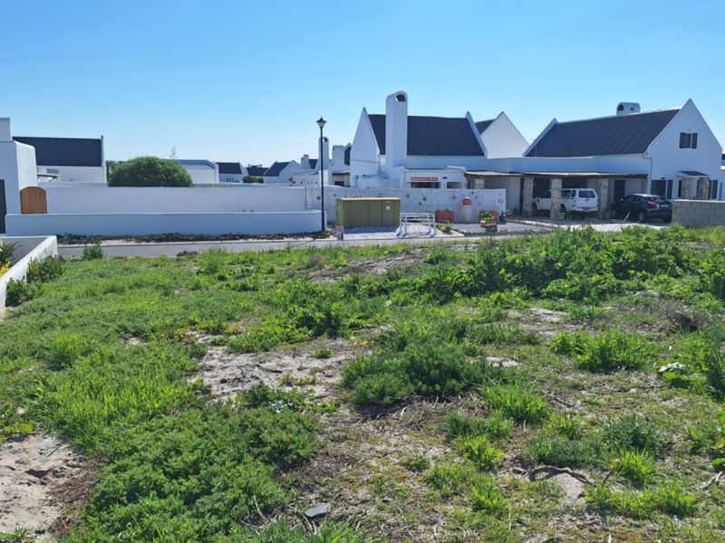 A vacant residential plot of land situated in a developed estate, featuring natural vegetation and surrounding boundary walls.