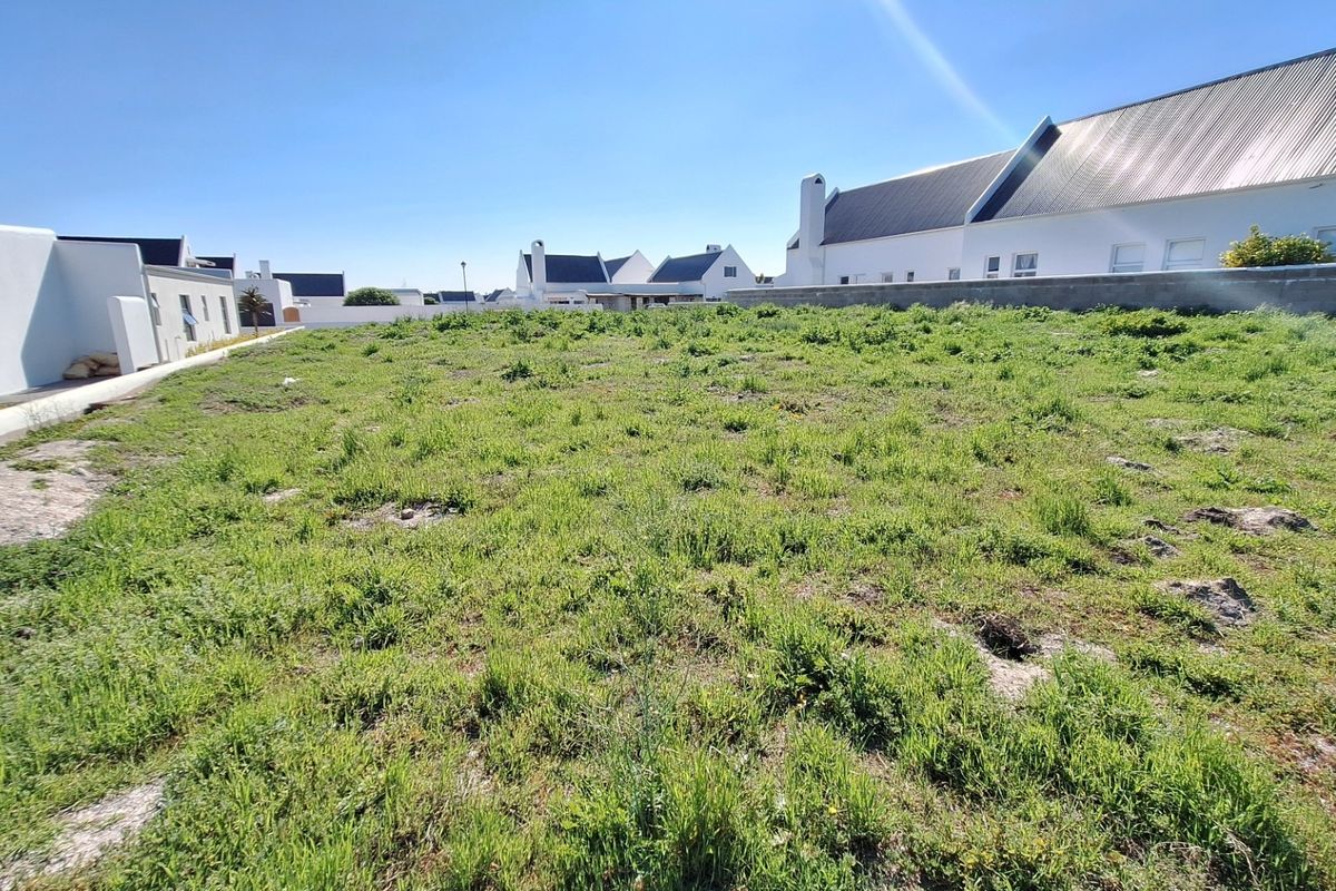 A vacant residential plot of land featuring natural grass cover and surrounding boundary walls in a developed residential estate.