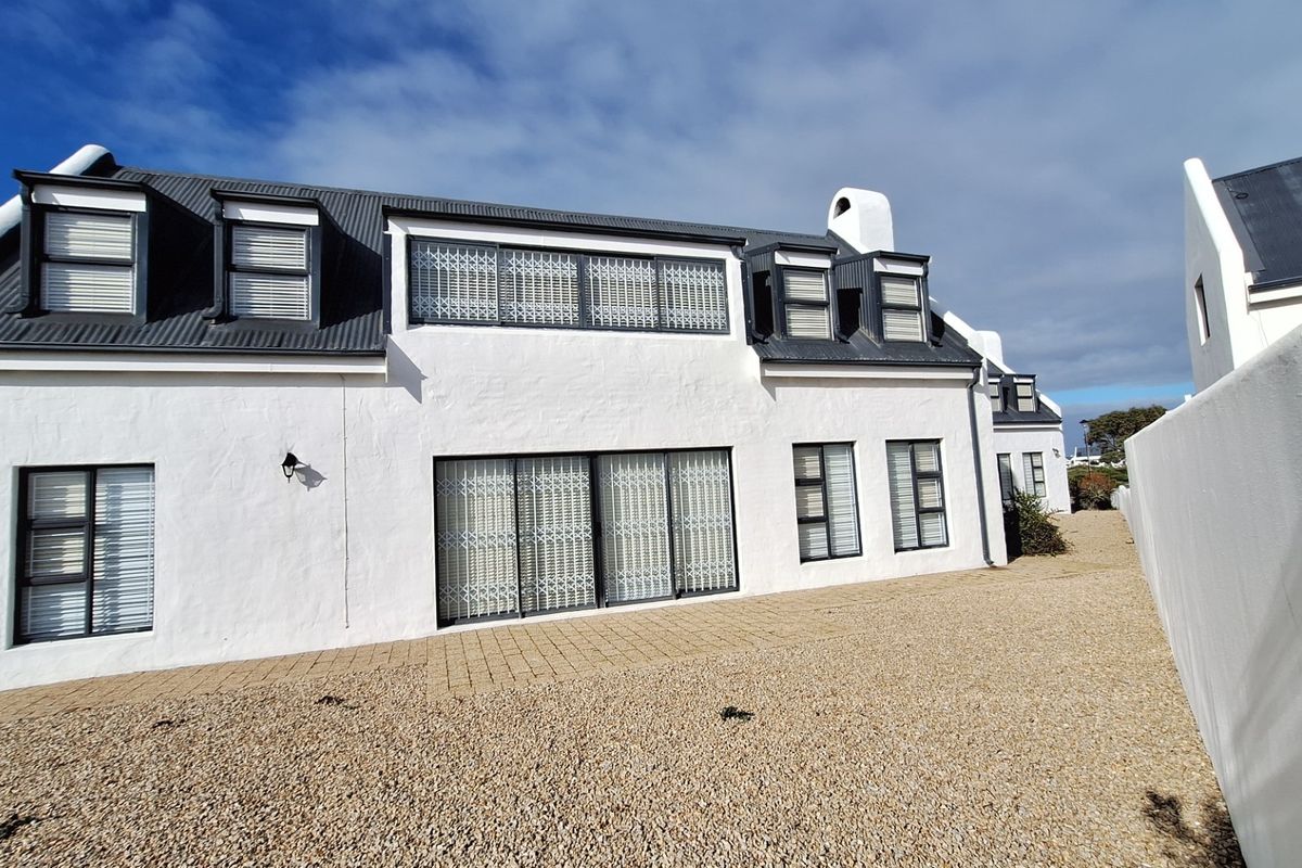 Rear elevation of a white-painted house featuring a corrugated metal roof, dormer windows, and a paved patio area with gravel landscaping.