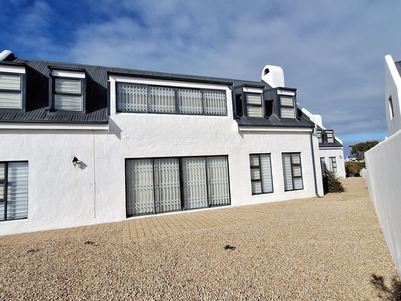 Rear elevation of a white-painted house featuring a corrugated metal roof, dormer windows, and a paved patio area with gravel landscaping.