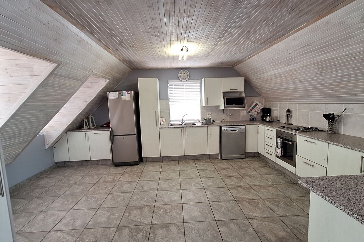 Spacious attic-style kitchen featuring light-toned cabinetry, granite countertops, built-in oven, gas hob, and distinctive timber-clad vaulted ceilings.