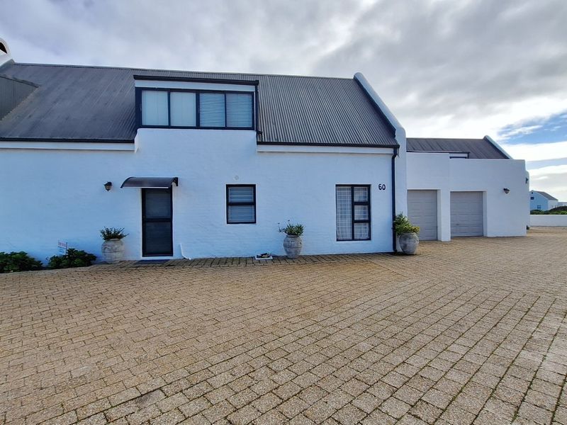A well-maintained white house featuring a corrugated metal roof, dormer windows, and a spacious paved driveway leading to a double garage.