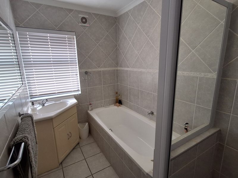 A functional bathroom featuring a built-in vanity, bathtub with shower screen, and neutral wall and floor tiling.
