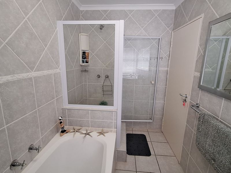 A functional bathroom featuring a built-in bathtub, a separate glass-enclosed shower, and neutral wall and floor tiling.