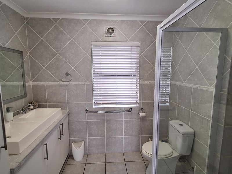 A well-maintained bathroom featuring a vanity with integrated basin, a glass-enclosed shower, a toilet, and neutral tiled finishes throughout.