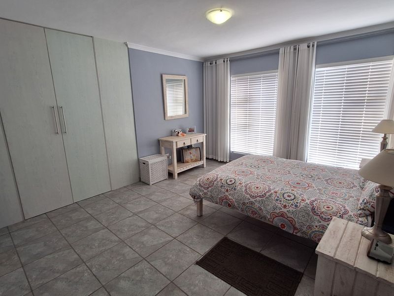 A well-maintained bedroom featuring neutral tiled flooring, ample built-in cupboard storage, and large windows fitted with venetian blinds for natural light control.