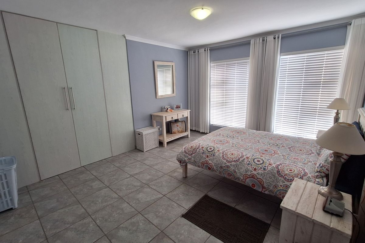 A well-maintained bedroom featuring neutral tiled flooring, ample built-in cupboard storage, and large windows fitted with venetian blinds for natural light control.