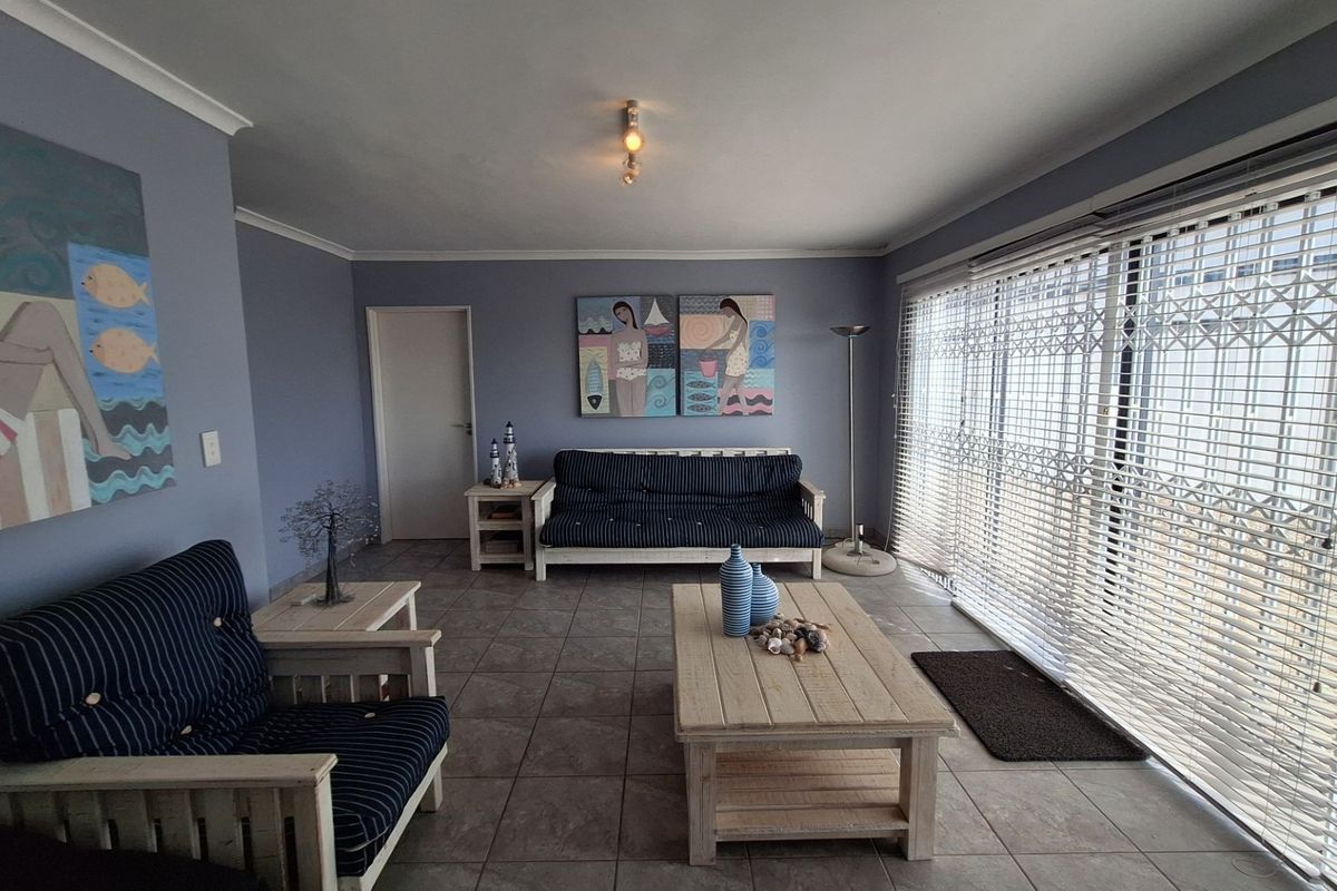 A spacious living room featuring tiled flooring, large sliding glass doors with security gates, and venetian blinds, offering a bright and functional living space.