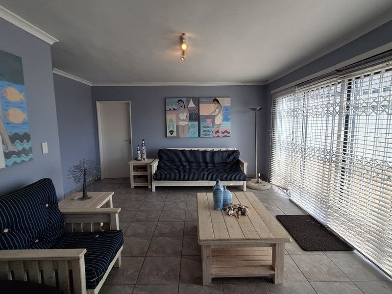 A spacious living room featuring tiled flooring, large sliding glass doors with security gates, and venetian blinds, offering a bright and functional living space.