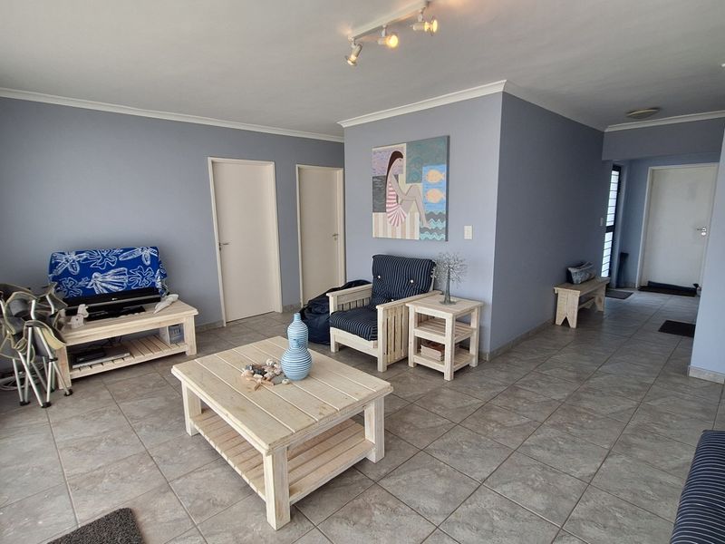 A spacious living room featuring neutral tiled flooring, track lighting, and clean wall finishes, providing a versatile area for relaxation.