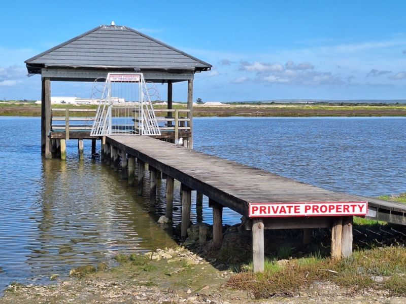 A wooden jetty extending into the water, featuring a covered gazebo structure and a metal security gate.