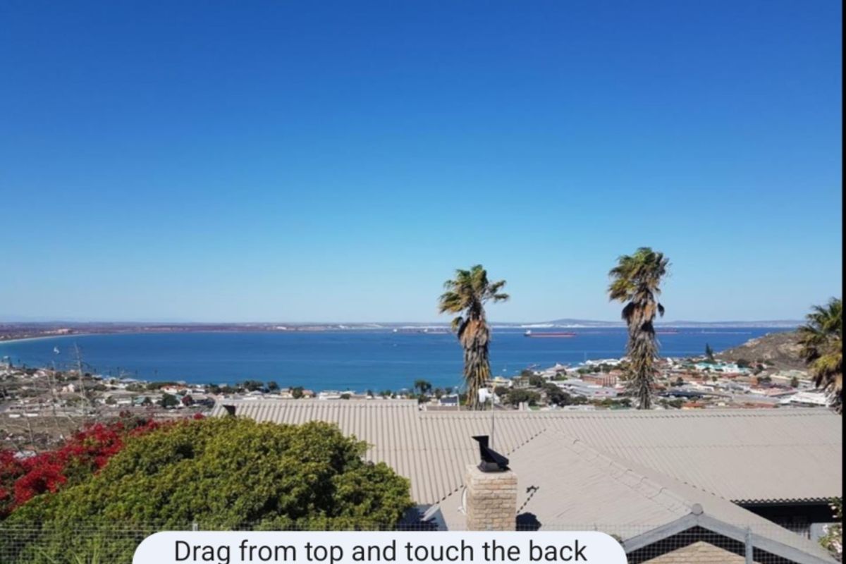 Elevated coastal view overlooking the bay and surrounding residential area, featuring a clear horizon and blue sky.