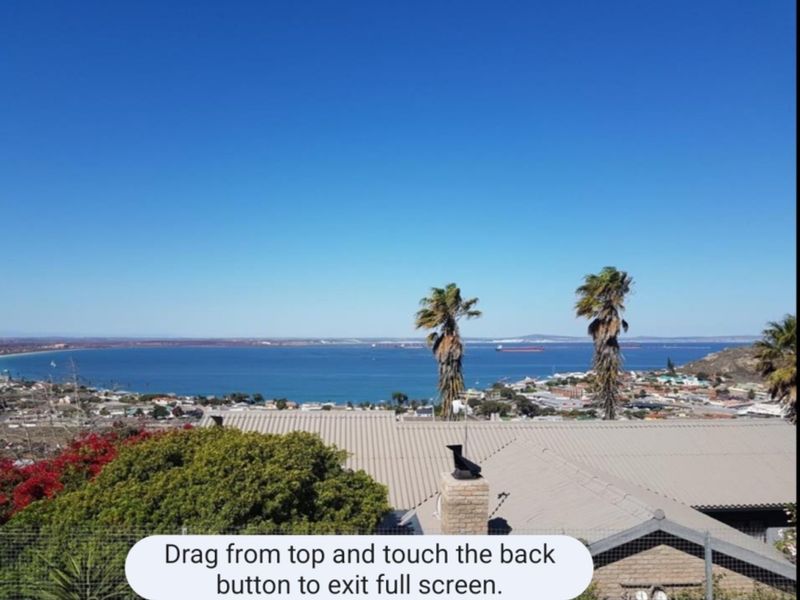 Elevated coastal view overlooking the bay and surrounding residential area, featuring a clear horizon and blue sky.