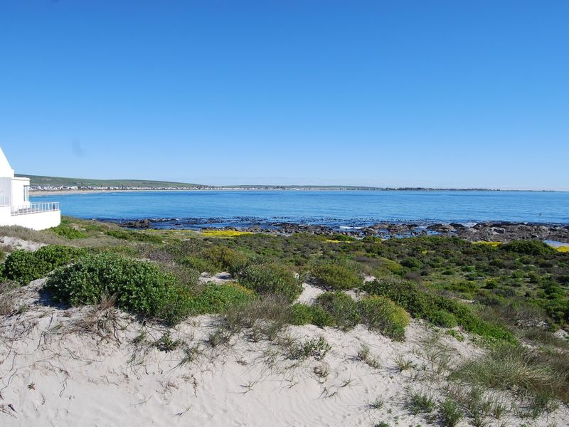 A scenic view of the coastline featuring natural sand dunes, native vegetation, and an expansive ocean outlook adjacent to a residential property.
