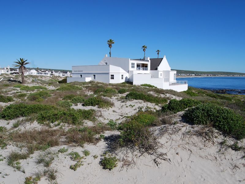 A scenic view of a white coastal property situated on a sandy dune overlooking the ocean.