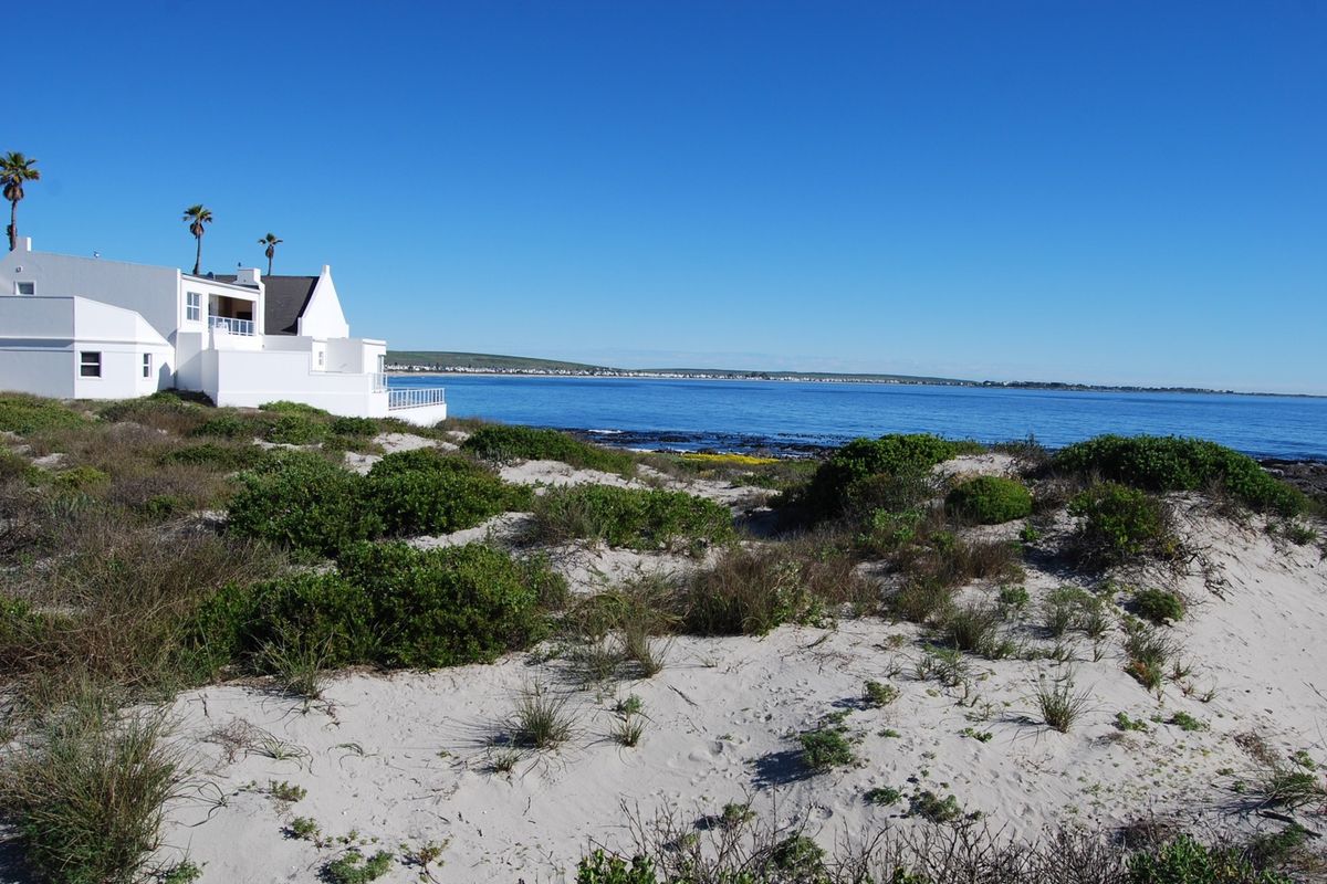 A scenic view of the coastline featuring sandy dunes, native vegetation, and a clear ocean outlook with a neighboring property visible in the distance.