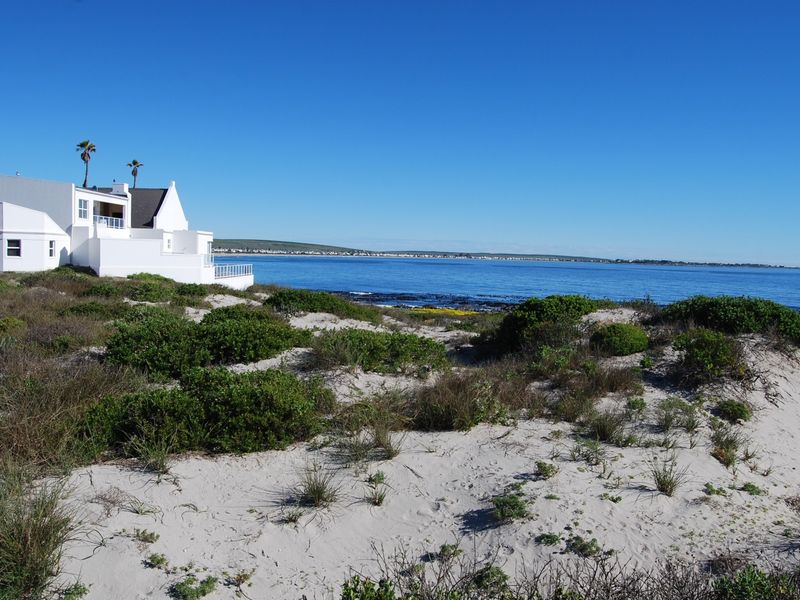 A scenic view of the coastline featuring sandy dunes, native vegetation, and a clear ocean outlook with a neighboring property visible in the distance.