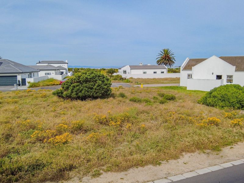 An aerial view of a vacant residential plot situated within an established coastal neighborhood, surrounded by existing homes.