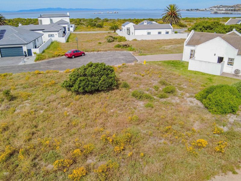 An aerial view of a vacant residential plot situated in a coastal estate, featuring natural vegetation and proximity to the ocean.