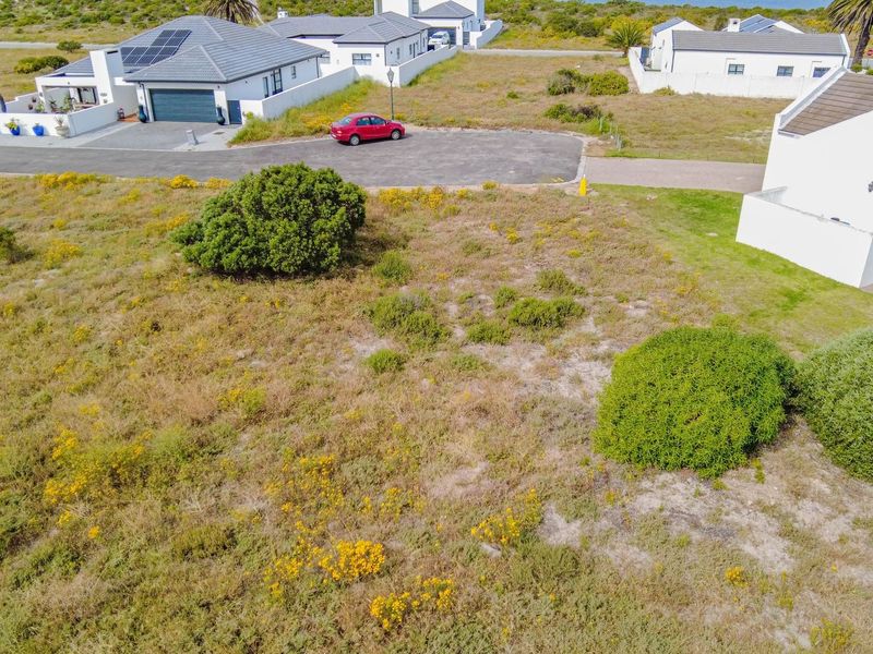 An aerial view of a vacant residential plot featuring natural vegetation, situated in a developed neighborhood with paved road access.