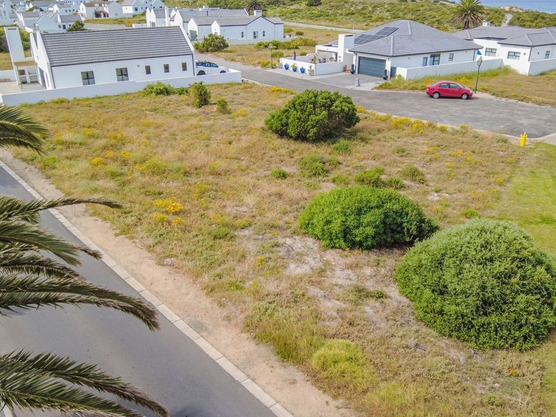 An elevated aerial view of a vacant residential plot situated in a developed coastal estate, featuring established road access and surrounding residential properties.