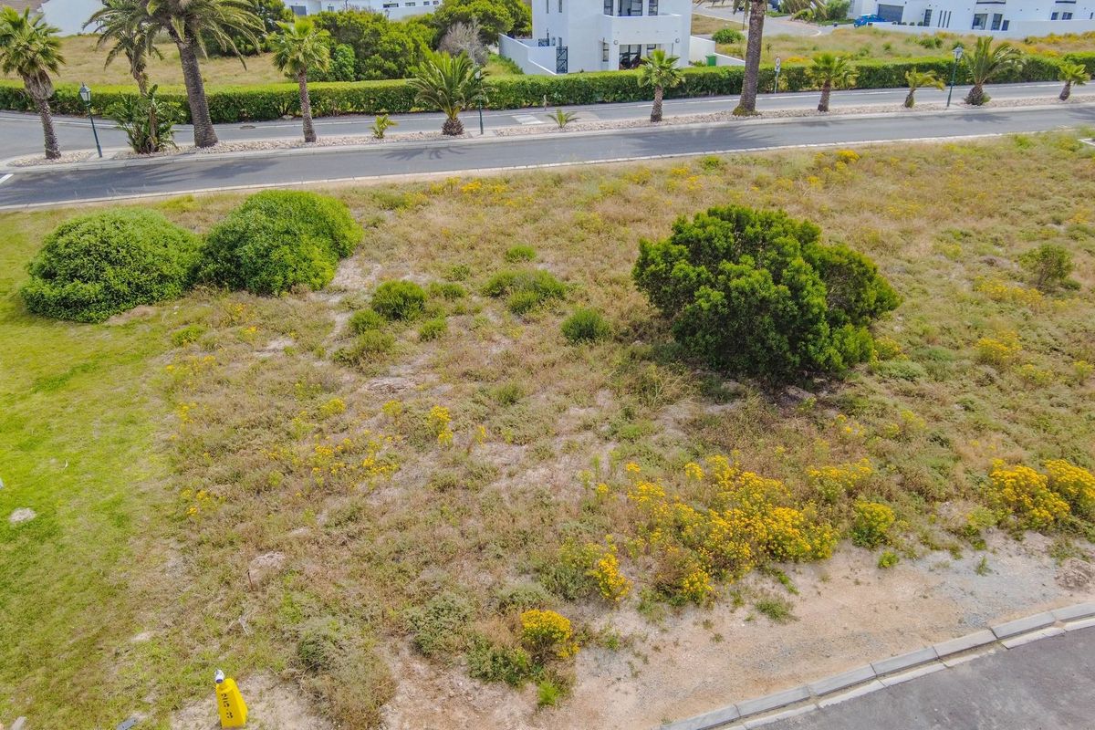 An aerial view of a vacant residential plot featuring natural vegetation, street access, and surrounding established neighborhood infrastructure.