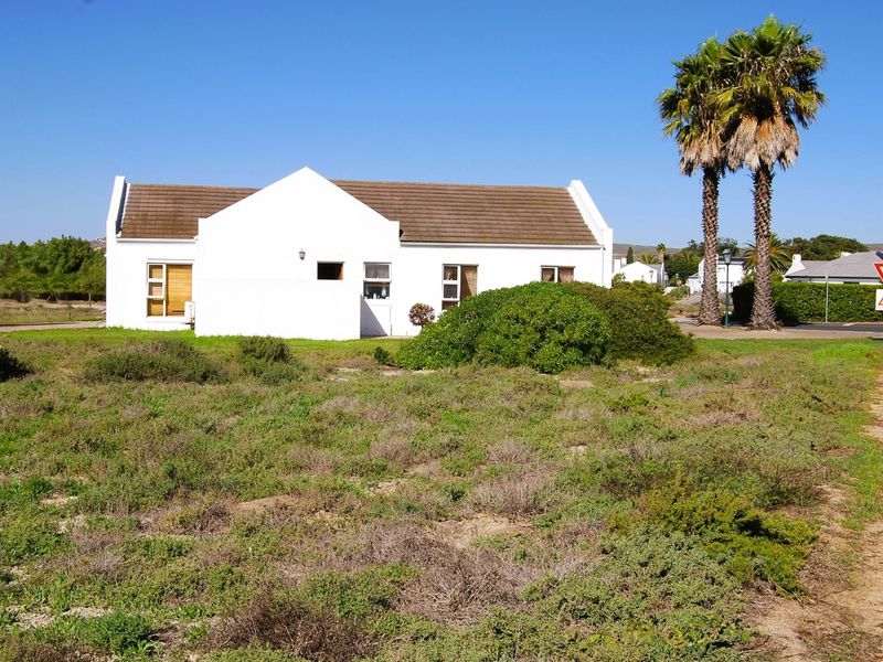 A view of the front facade of a white residential building with a tiled roof, situated on a large plot of land.