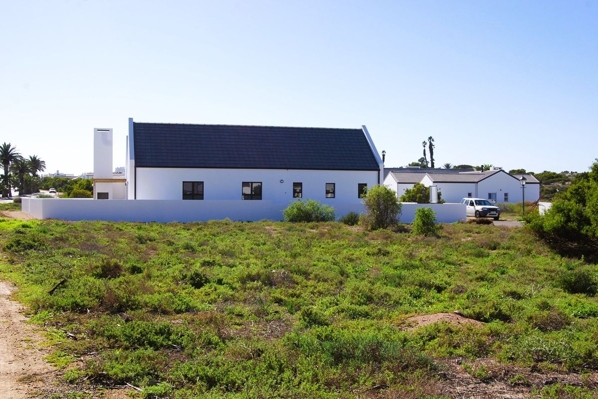 A view of the rear elevation of a white residential building with a dark tiled roof, featuring a boundary wall and surrounding natural vegetation.