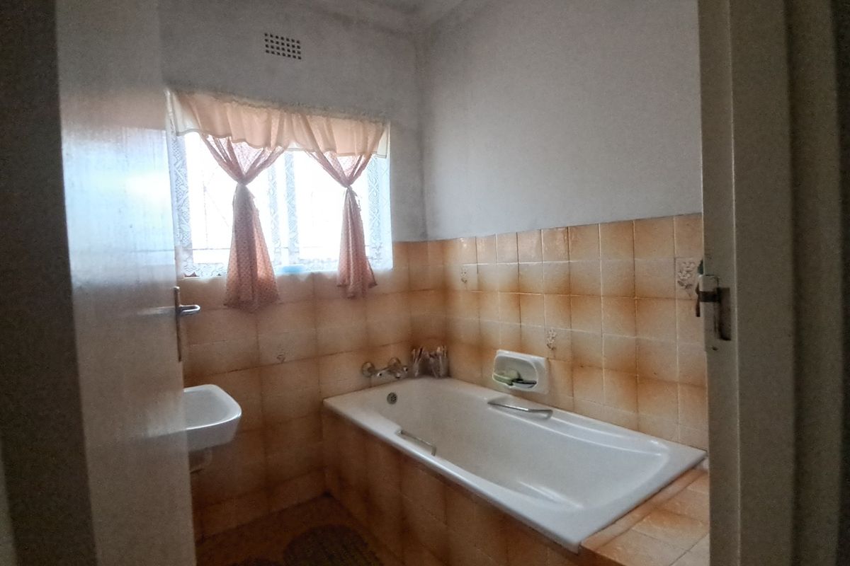 A dated bathroom featuring a standard bathtub, wall-mounted basin, and original ceramic wall tiling, offering potential for a modern renovation.