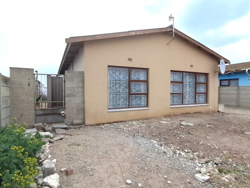 Front elevation of a single-story house featuring metal-framed windows with security bars, a precast concrete boundary wall, and an unpaved front yard area.