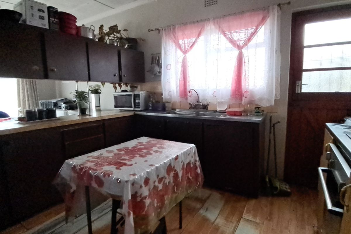 A dated kitchen featuring dark laminate cabinetry, timber flooring, and a double bowl stainless steel sink with a window view.