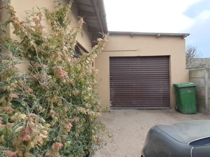 Exterior view of a single garage featuring a brown roller shutter door and adjacent concrete boundary wall.