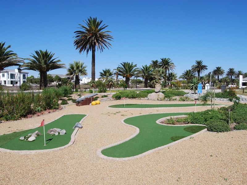 A well-maintained miniature golf course facility featuring synthetic putting greens, landscaped garden areas, and paved walkways within a residential estate setting.