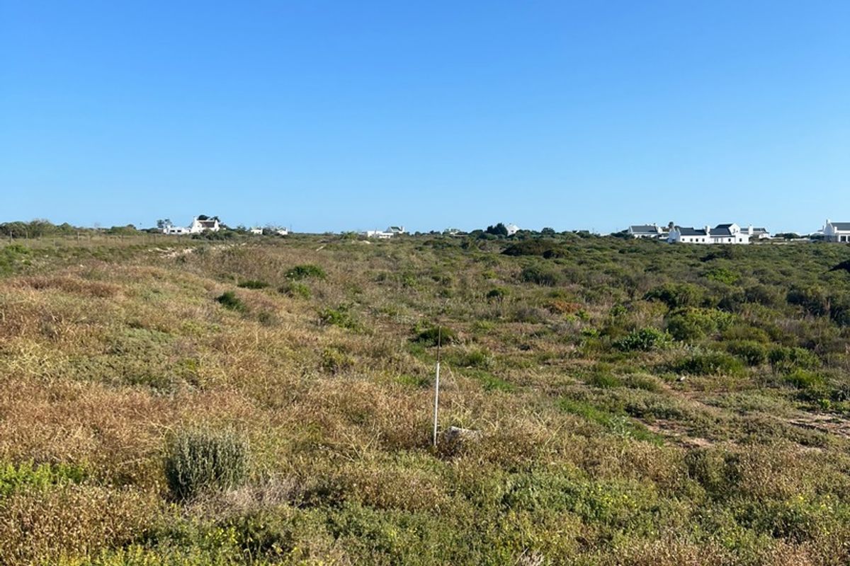 A view of a vacant residential plot featuring natural coastal vegetation and surrounding neighborhood homes in the distance.